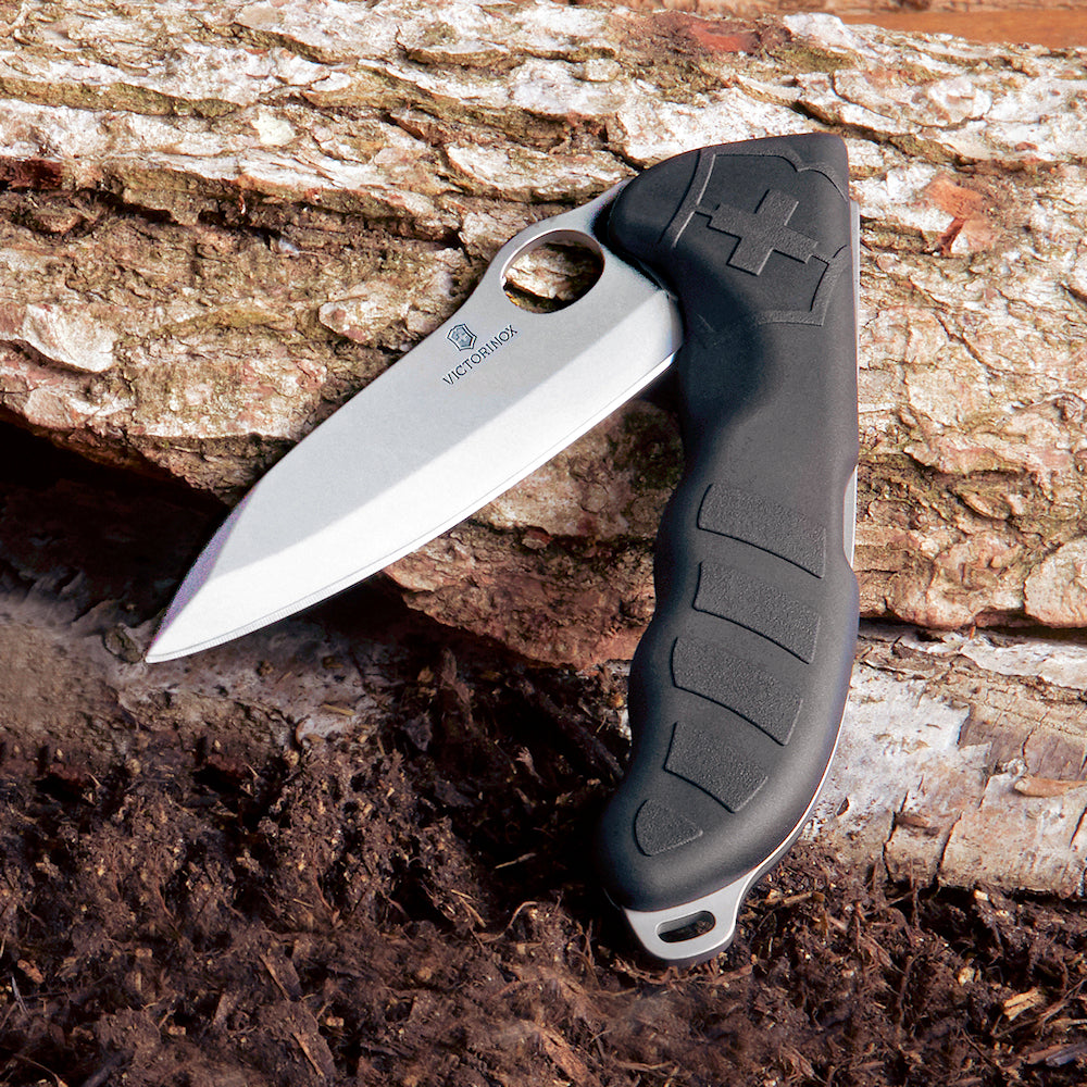 Victorinox Hunter Pro Metsästysveitsi - Musta Veitsi Vyöllä, asetettu puunrungolle, korostaa sen kestävyyttä ja ulkokäyttöä.
