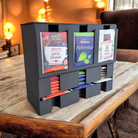 Teepussiannostelija, 3 lokeroa, täytetty eri teelaaduilla, sijoitettuna olohuoneen pöydälle. Hygieeninen ja ympäristöystävällinen säilytysratkaisu.