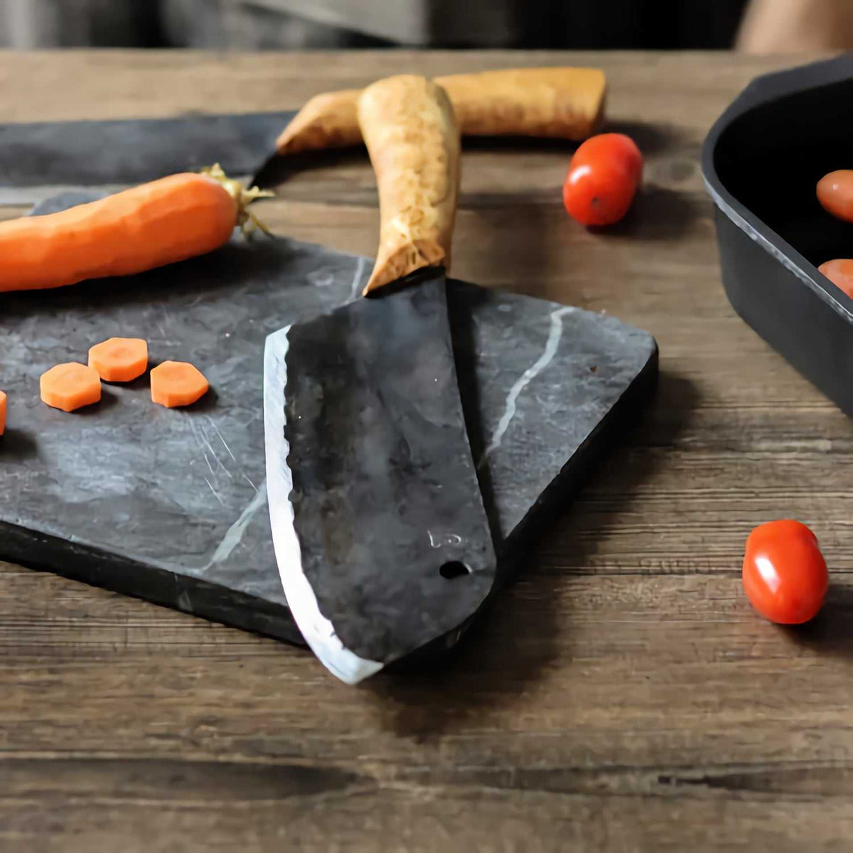 Laatupuukko kokkiveitsi leikkuulaudalla, ympärillä porkkanoita ja tomaatteja. Täydellinen veitsi ruoanvalmistukseen.