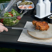 Westmark grillilasta käytössä ulkogrillauksessa, nostamassa grillattua lihaa lautaselle puutarhapöydällä.